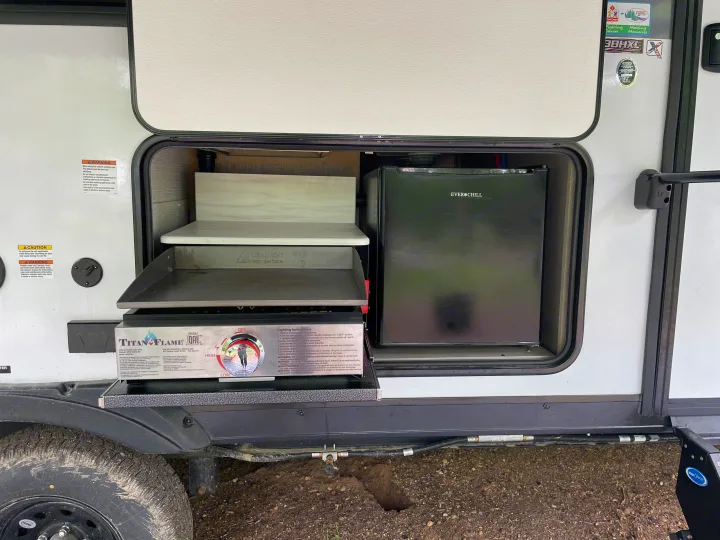 Explore this RV rental's outdoor kitchen: Titan Flame flat-top grill, Ever Chill mini-fridge, and counter area.. Forest River Wildwood X-Lite Platinum 2024
