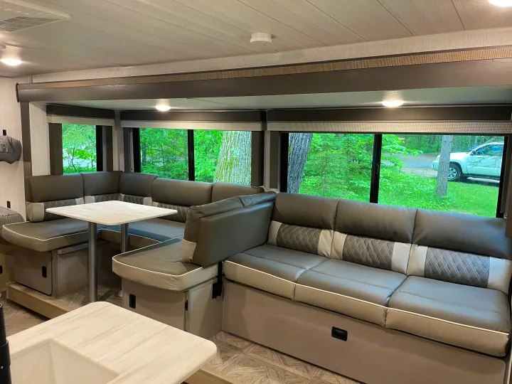 Inside an RV rental: a cozy, modern dinette with a large U-shaped sofa, table, and scenic views through wide windows.. Forest River Wildwood X-Lite Platinum 2024