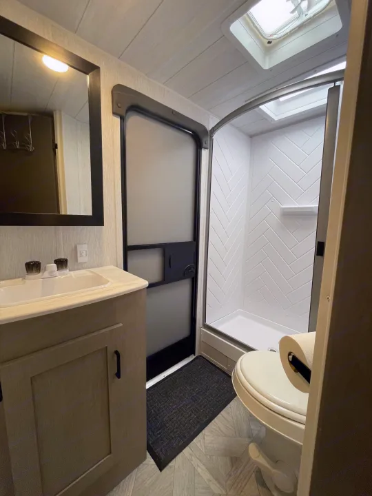 Compact RV rental bathroom featuring a sink vanity, mirror, toilet, and shower stall with a skylight.. Forest River Wildwood X-Lite Platinum 2024