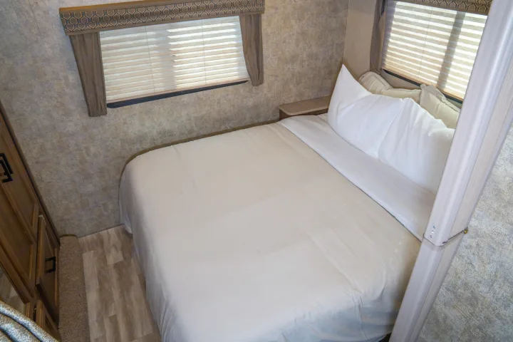 Experience comfort in this RV rental bedroom: a clean bed with white linens, two windows, and practical built-ins.. Gulf Stream Conquest 2019