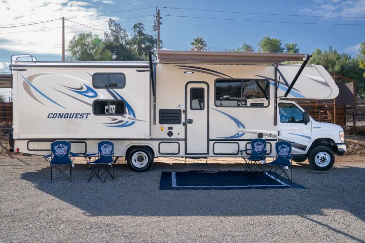 This Gulf Stream Conquest RV rental shows its extended awning, four chairs, and mat on a gravel lot.. Gulf Stream Conquest 2019