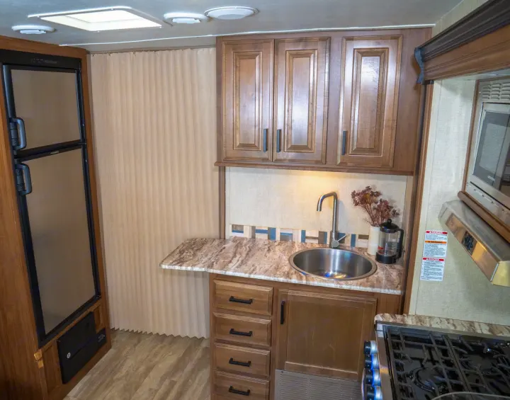 This RV rental showcases a compact and functional kitchen, featuring a fridge, sink, stove, microwave, and wood-look cabinets.. Gulf Stream Conquest 2019