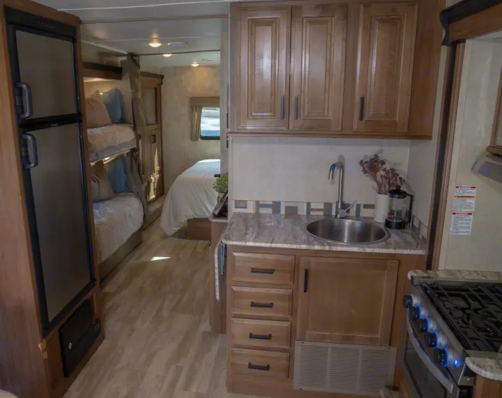 Spacious rv rental interior featuring a kitchen with sink and stove, bunk beds, and a master bedroom in the background.. Gulf Stream Conquest 2019