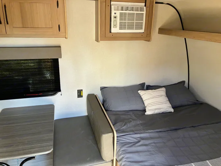 Cozy RV rental interior with bed, dinette, window, and wall-mounted AC unit, perfect for compact travel.. Coleman 17B 2025