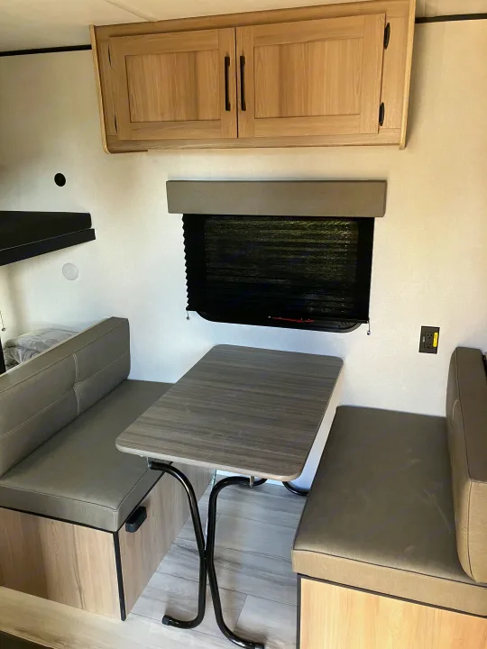 RV rental: Bright interior with a grey dinette, wood-look table, overhead cabinets, window with blind, and partial view of a bunk.. Coleman 17B 2025