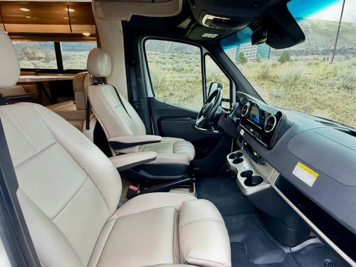 Bright interior of an RV rental camper van's cockpit area, featuring light-colored driver and passenger seats.. Thor Tiburon 2022