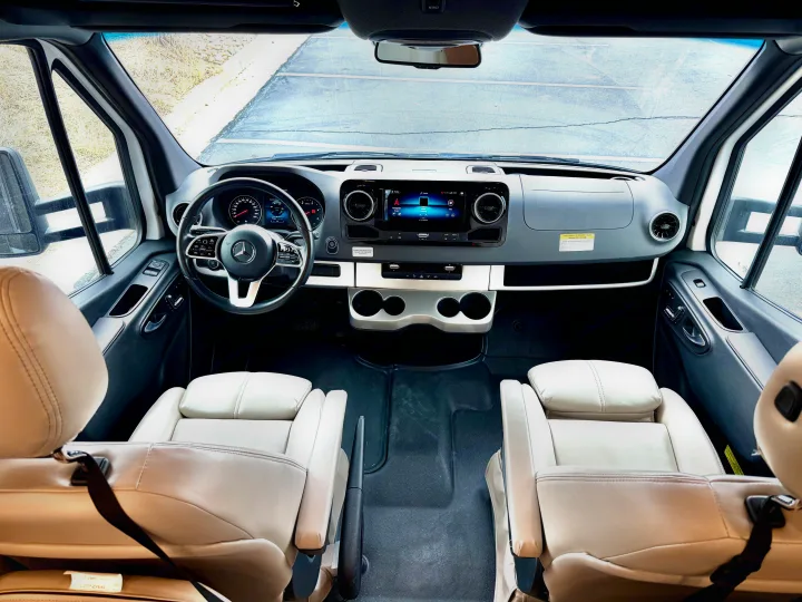 Plush light seats, modern dashboard, and steering wheel in this spacious RV rental cockpit. Ready for your journey.. Thor Tiburon 2022