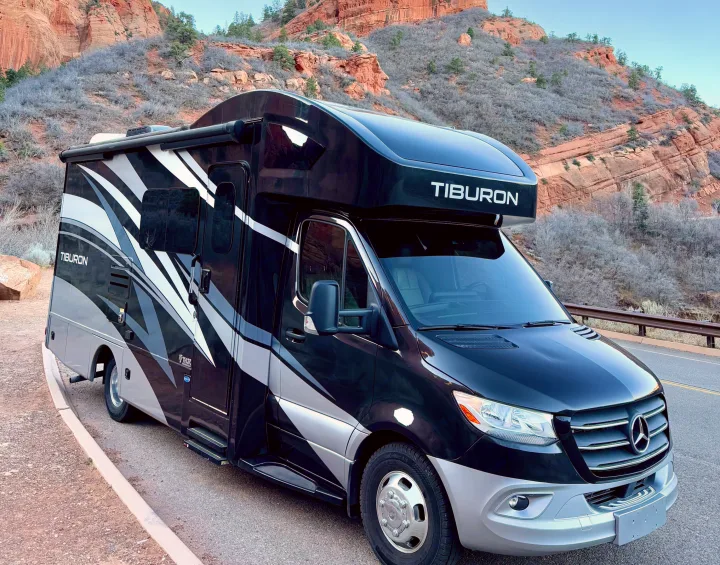 Black and grey Thor Tiburon RV rental by red rock mountains, parked roadside for scenic adventures.. Thor Tiburon 2022