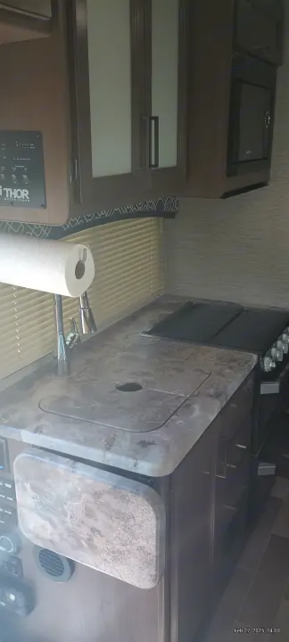 Compact RV rental kitchen with a mottled gray countertop, covered sink, stove, microwave, and brown cabinetry, ideal for travel.. Thor Motor Coach Chateau 2021