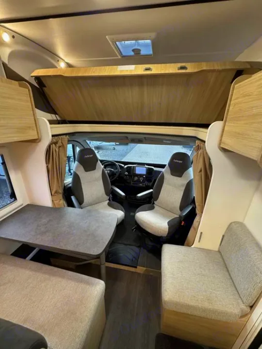 Modern rv rental interior showing front cockpit seats, dining table with benches, and an overhead drop-down bed.. Challenger C194 START EDITION 2025