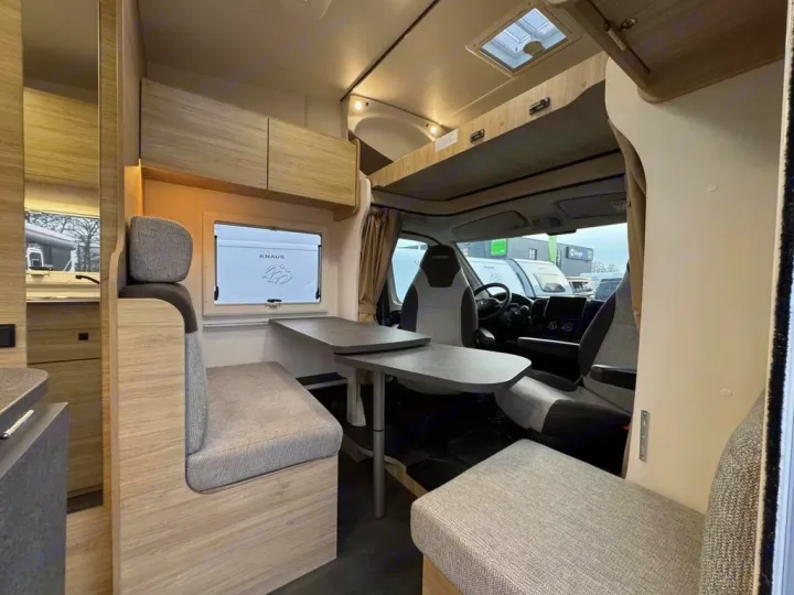 Modern rv rental interior: light-wood dinette, grey cushions, compact kitchen counter, and front cabin area visible.. Challenger C194 START EDITION 2025