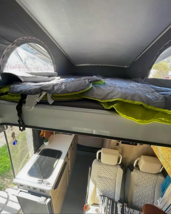 Interior of an RV rental showing the elevated pop-top bed, a compact kitchenette, and front seats below. Ideal camper setup.. Dodge Winnebago 2021
