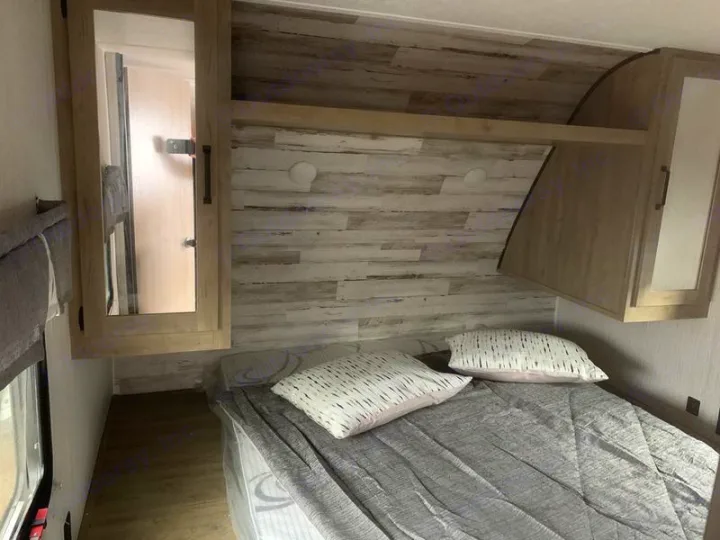Modern RV rental bedroom featuring a bed, wood-look walls, and overhead storage. Ideal for comfortable travel.. Forest River Palomino Puma XLE 2022