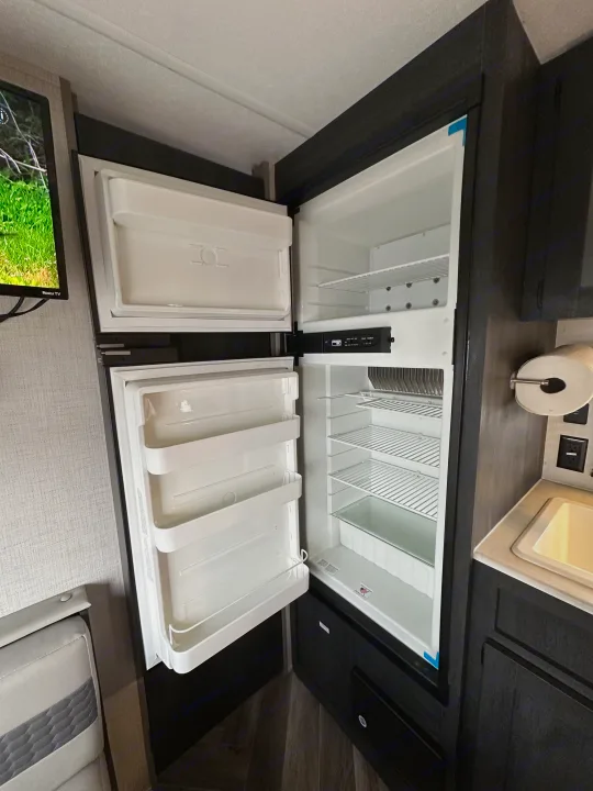 Spacious, open refrigerator in an RV rental, ready for provisions. Features freezer, shelves, and crisper.. Ozark Lite 2021