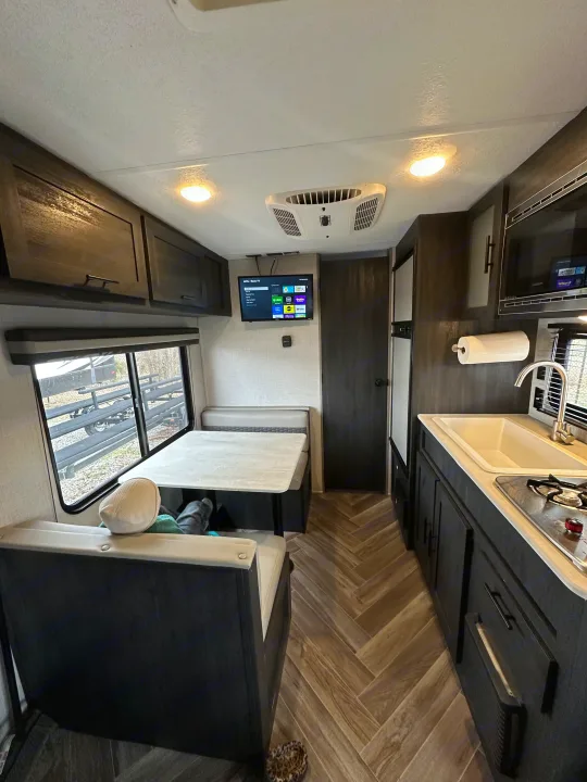 This RV rental showcases its interior with a kitchen (sink, stove, microwave), dinette, TV, & overhead storage. Clean & modern.. Ozark Lite 2021