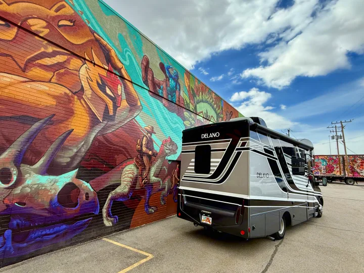 Sleek Delano RV rental parked beside a vibrant mural of a person riding a dinosaur. Adventure awaits!. Thor Delano 2023