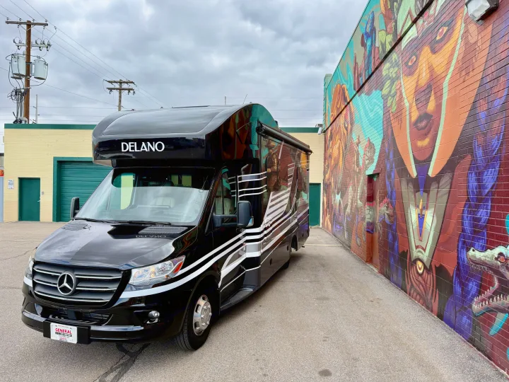 Black RV rental with white stripes, parked alongside a vibrant mural on a brick wall. Ready for your adventure.. Thor Delano 2023