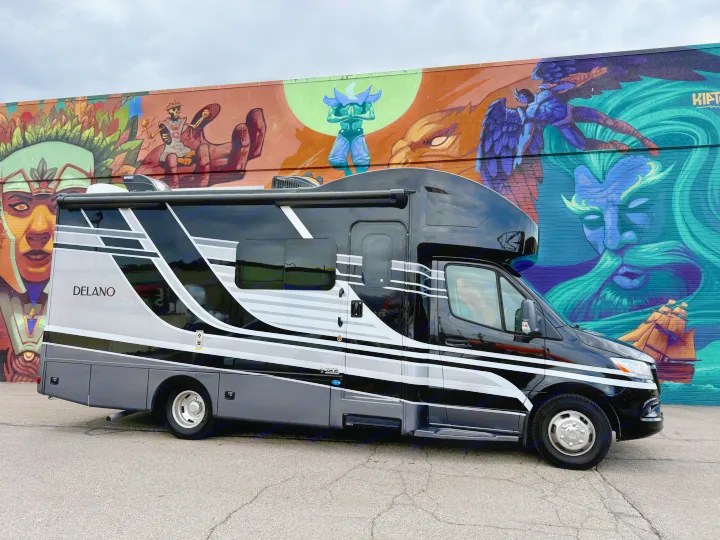 This sleek black & gray RV rental is parked against a vibrant mural depicting diverse fantasy characters.. Thor Delano 2023