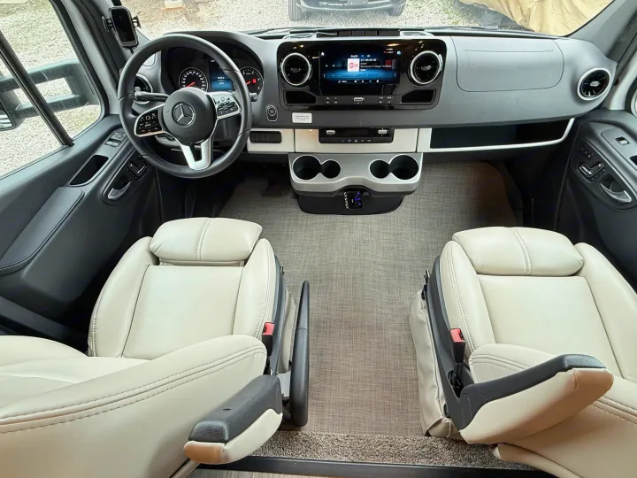 Spacious RV rental interior: Mercedes-Benz cockpit with light leather seats, dashboard, and infotainment system for comfortable travel.. Thor Delano 2023