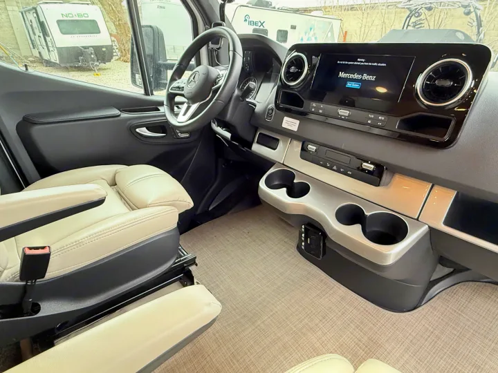 Modern Mercedes-Benz Sprinter RV rental interior, featuring the dashboard, cream captain's seats, and center console.. Thor Delano 2023