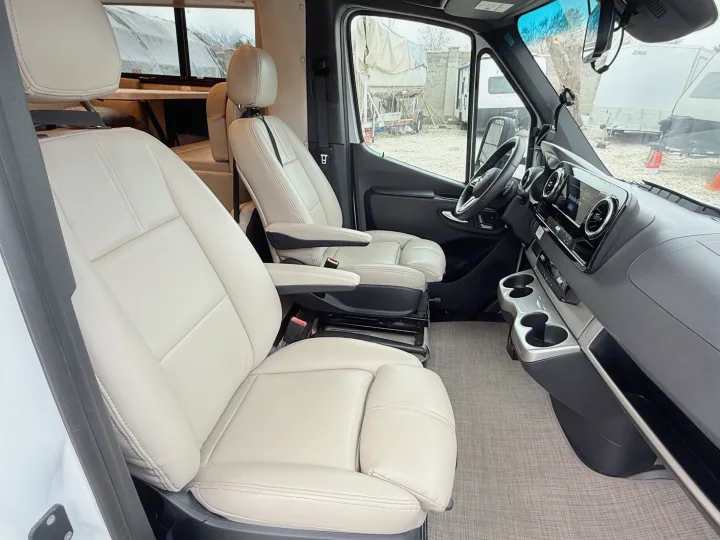Inside an rv rental: inviting front cabin with light-colored, plush captain's chairs and modern dashboard controls.. Thor Delano 2023