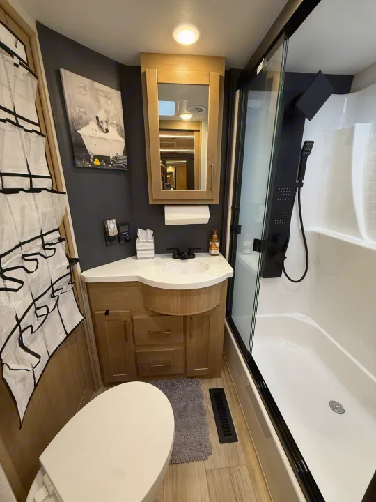 Compact yet well-appointed RV rental bathroom with a white toilet, light wood vanity & mirror, and sleek black shower.. Heartland Cyclone 2025
