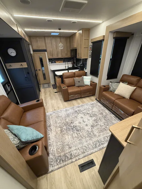 Spacious RV rental with inviting living area and full kitchen, featuring comfortable brown seating and modern lighting.. Heartland Cyclone 2025