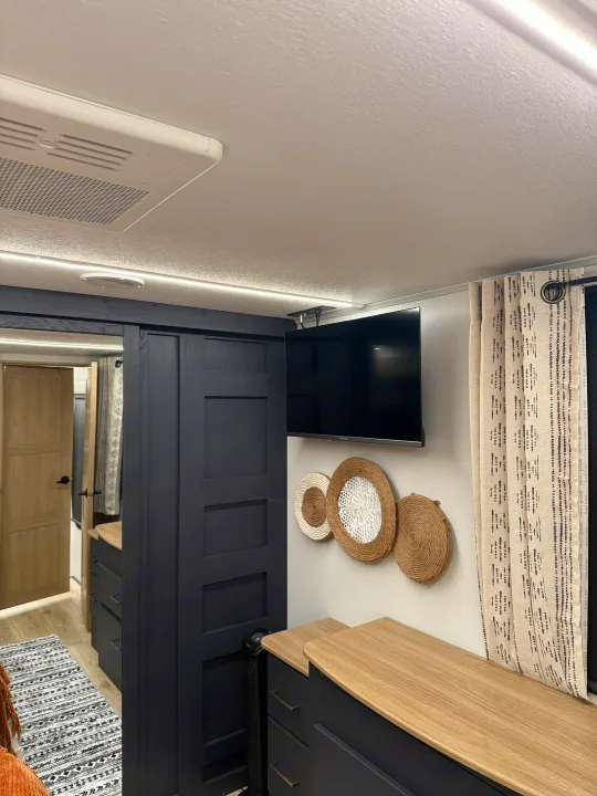 RV rental: Brightly lit interior bedroom with TV, sleek black storage, light wood counters & decorative wall art.. Heartland Cyclone 2025