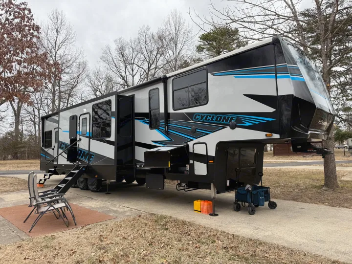Spacious gray, black, and blue Cyclone fifth-wheel RV rental set up at a campground, featuring chairs and accessories for outdoor living.. Heartland Cyclone 2025