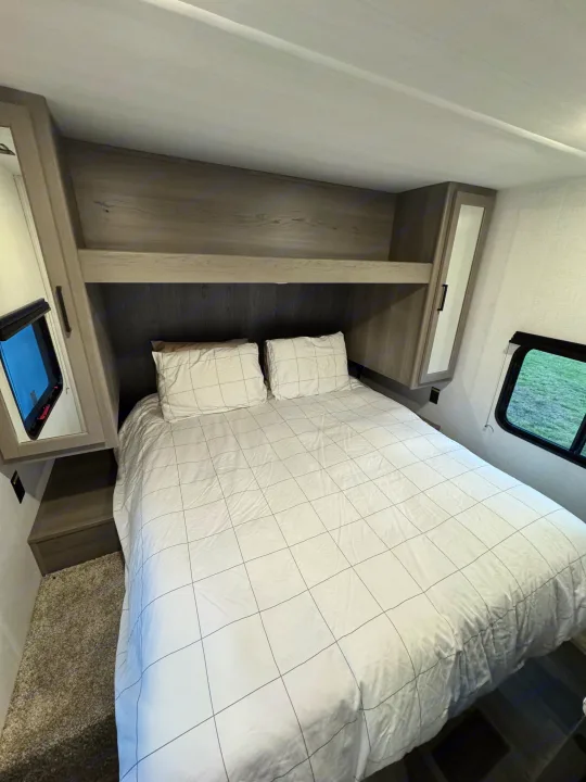 Compact RV rental bedroom interior with grid bedding, built-in storage, and windows for travel.. Keystone RV Hideout 2024