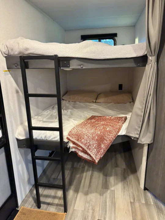 RV rental bunk beds: a cozy interior sleeping area with ladder, blankets, pillows, and a window.. Keystone RV Hideout 2024