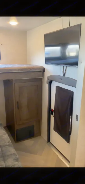RV rental interior featuring a bunk bed, wall-mounted TV, and an open rear access door with a cover.. Forest River Wildwood 2021