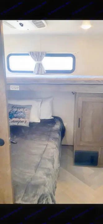 RV rental features cozy bunk beds, a windowed upper bunk, and a lower bed with a "Happy Camper" pillow.. Forest River Wildwood 2021