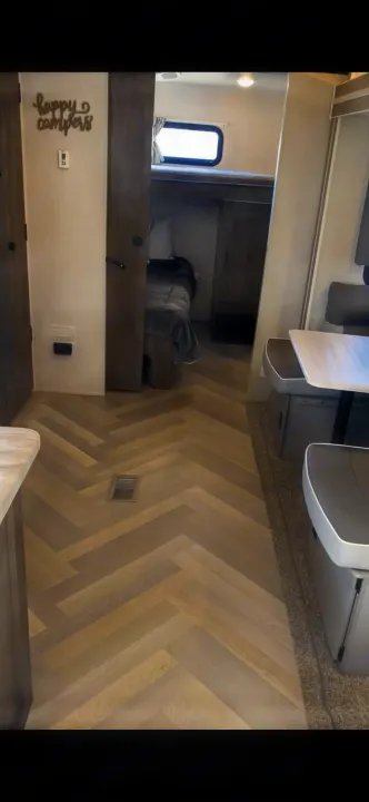 Inside an RV rental: light herringbone flooring extends towards cozy bunk beds with a window and a practical dinette.. Forest River Wildwood 2021