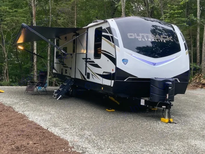 A pristine white and black 'Outback Ultra-Lite' travel trailer is parked on a gravel site, ready for an RV rental getaway.. Keystone RV Outback Ultra-Lite 2021