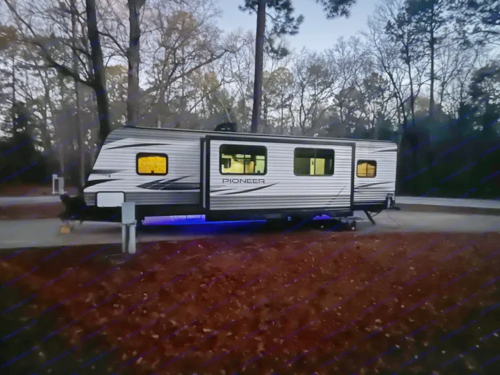 Night view of a Pioneer RV rental parked at a campsite, with illuminated interior and blue underglow.. Heartland RVs Pioneer 2020