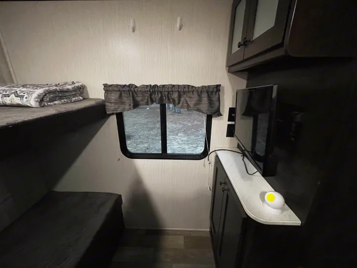 Inside this RV rental, find a comfortable bunk bed, window with outdoor view, TV, and dark wood storage cabinets.. Heartland RVs Pioneer 2020