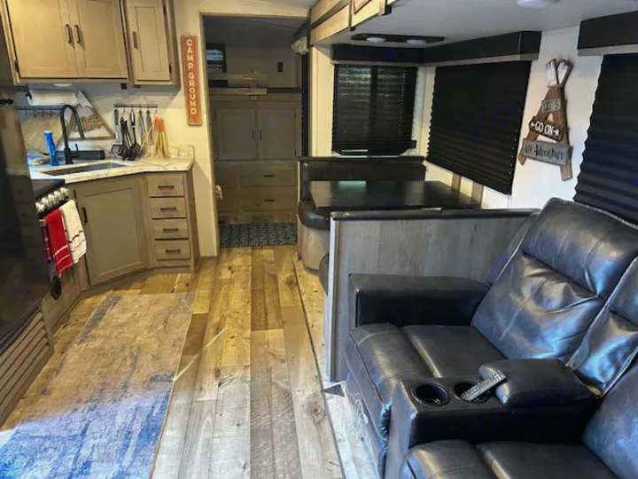 Inside a modern RV rental: a kitchen with sink, dining booth, and comfy recliners with cup holders.. Keystone RV Outback Ultra-Lite 2021