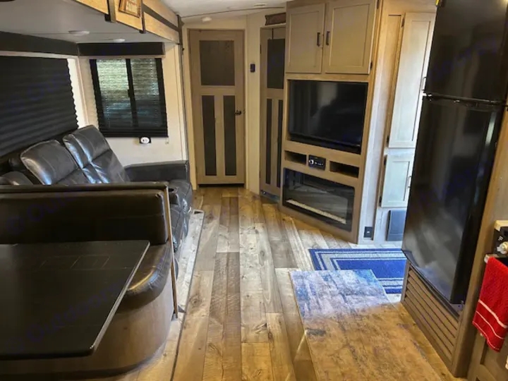 Spacious RV rental interior with a comfy sofa, entertainment center (TV, fireplace), refrigerator, and dining table.. Keystone RV Outback Ultra-Lite 2021