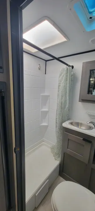 Clean and compact RV rental bathroom, featuring a tiled shower, sink vanity, toilet, and bright skylight.. Heartland RVs Mallard Pathfinder 2022