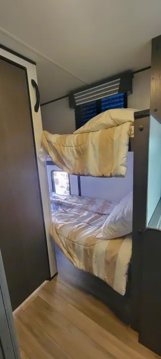Inside a clean RV rental: two compact bunk beds with striped bedding and pillows, next to a window with blinds.. Heartland RVs Mallard Pathfinder 2022