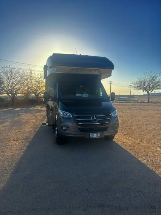 Dark brown Entegra Mercedes RV parked in a sunny, arid landscape, casting long shadows. Explore with this rv rental!. Entegra Coach Qwest 2020