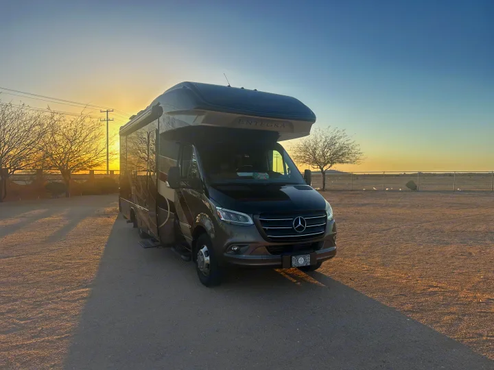 Dark brown Entegra Mercedes-Benz rv rental parked on a dirt lot under a glowing sunset sky. Perfect for desert adventures.. Entegra Coach Qwest 2020