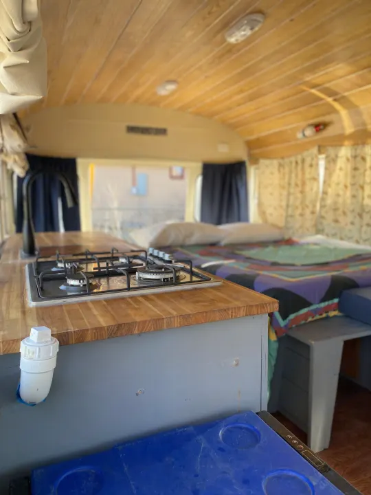 Functional RV rental interior featuring a kitchen with gas stove, wooden counter, and a comfortable bed setup.. GMC Vandura 1986