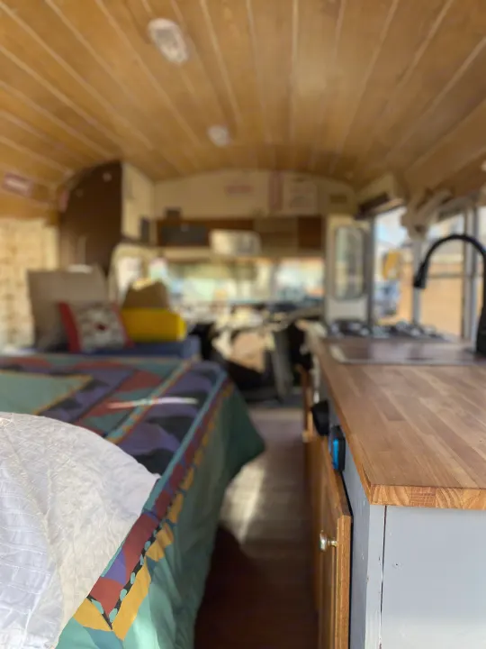 View from the bed in an RV rental, showing a colorful quilt, wood-paneled ceiling, and a full kitchen counter.. GMC Vandura 1986
