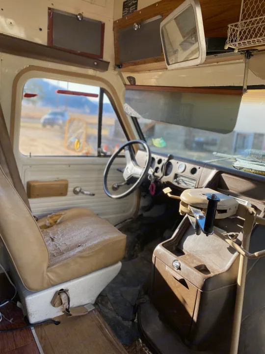 Experience a classic RV rental: the driver's interior with a worn seat, vintage dashboard, and clear road trip views.. GMC Vandura 1986