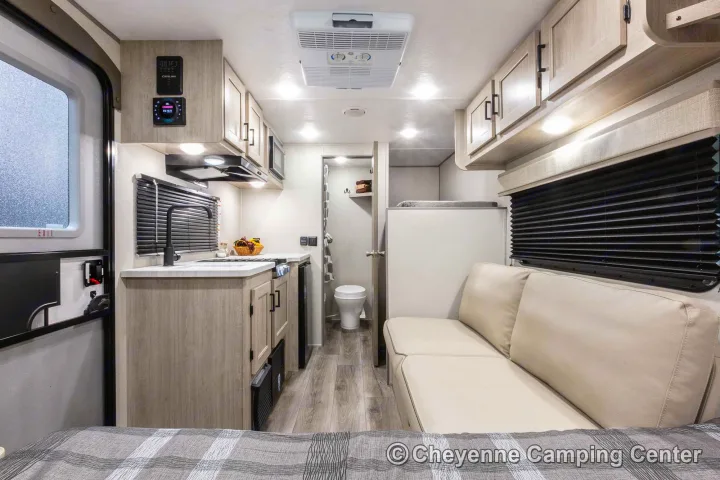 Modern rv rental interior with a light-toned kitchenette, comfy sofa, bed, and visible bathroom. Bright, compact living space.. Coachmen 164BHX 2023