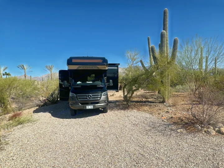 This RV rental is parked at a beautiful desert site, surrounded by tall saguaro cacti under a clear sky.. Entegra Coach Qwest 2020
