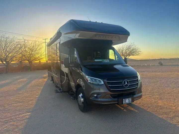 A sleek Mercedes-Benz Entegra RV rental gleams in golden light, ready for desert adventures at sunrise or sunset.. Entegra Coach Qwest 2020