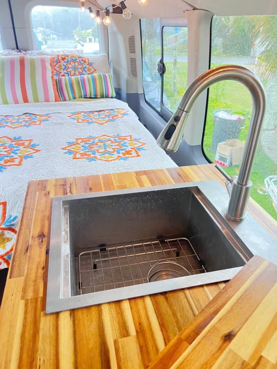 Cozy RV rental interior: colorful bed with pillows, and a wooden counter with a modern sink and faucet setup.. Ford Transit Custom 2016